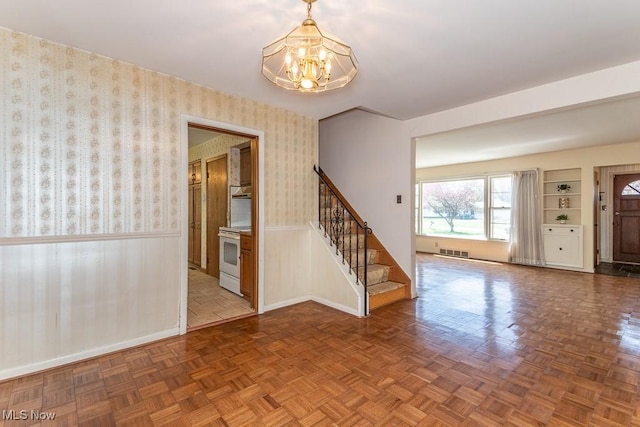 foyer with an inviting chandelier, a wainscoted wall, stairs, baseboards, and visible vents
