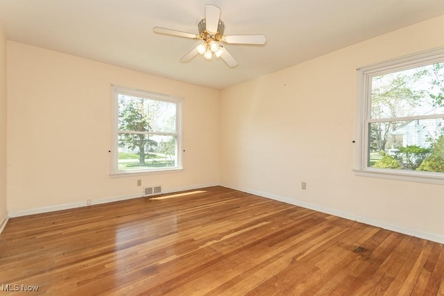 spare room featuring visible vents, baseboards, a wealth of natural light, and hardwood / wood-style floors