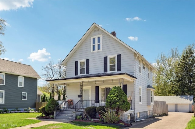 view of front of house featuring a detached garage, a front yard, an outbuilding, a chimney, and covered porch