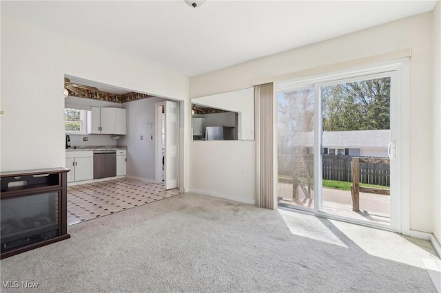 unfurnished living room featuring baseboards, light carpet, and a sink
