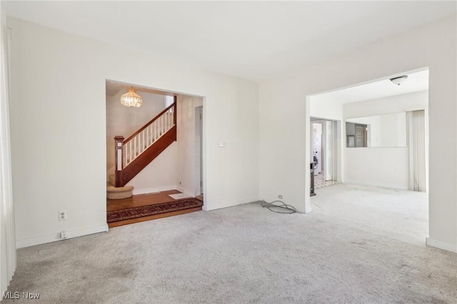 unfurnished living room featuring stairway, an inviting chandelier, and carpet flooring