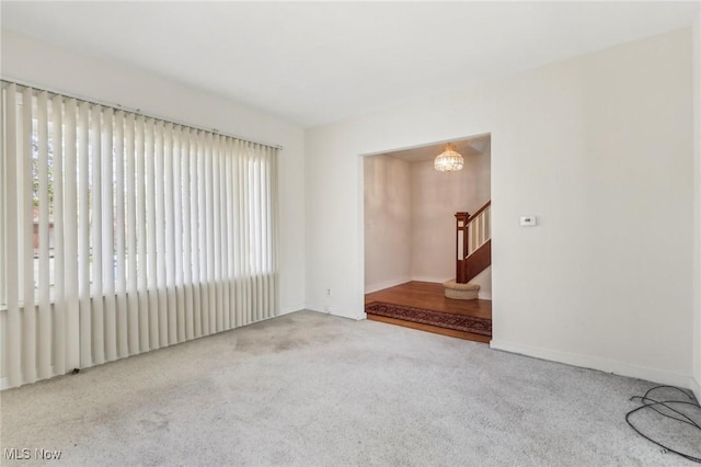carpeted spare room featuring stairs, baseboards, and a notable chandelier