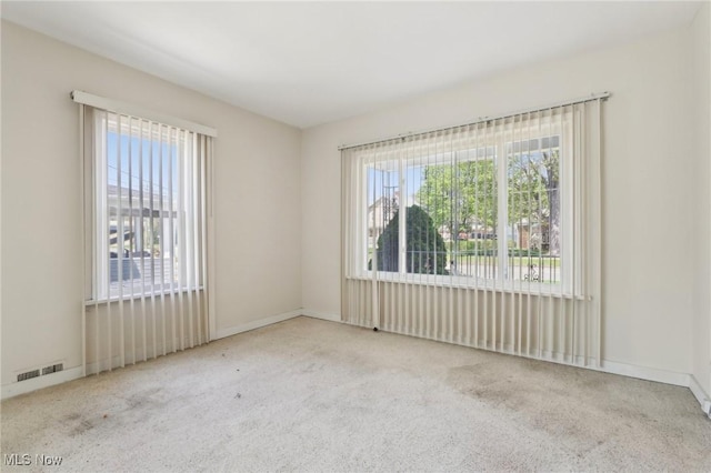 carpeted empty room featuring visible vents, baseboards, and a healthy amount of sunlight