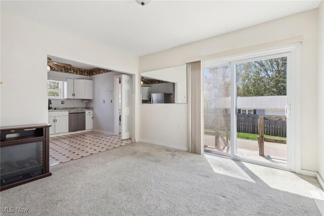 unfurnished living room with baseboards, a sink, and light carpet