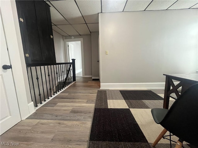 corridor with baseboards, a drop ceiling, wood finished floors, and an upstairs landing