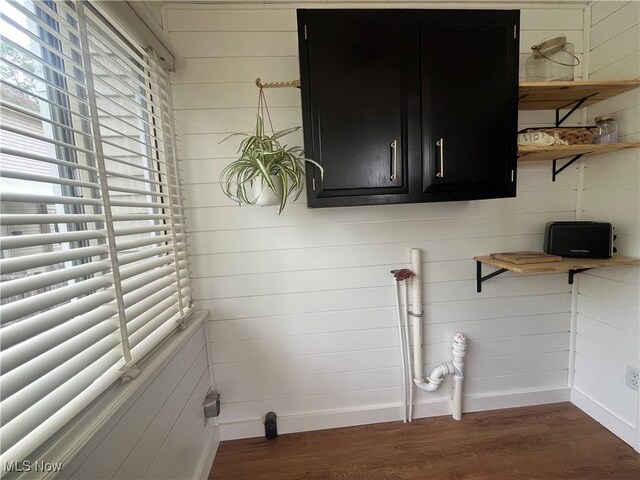 laundry room featuring baseboards, wood walls, and dark wood finished floors