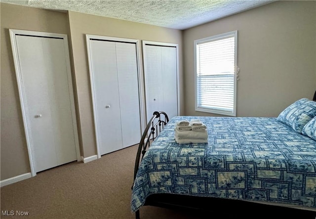 carpeted bedroom with baseboards, two closets, and a textured ceiling