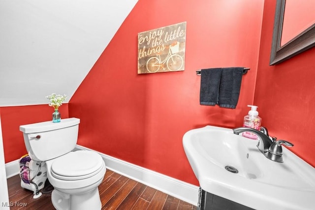 half bath with a sink, toilet, baseboards, wood finished floors, and lofted ceiling