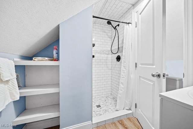 bathroom with a textured ceiling, wood finished floors, vaulted ceiling, and a shower stall