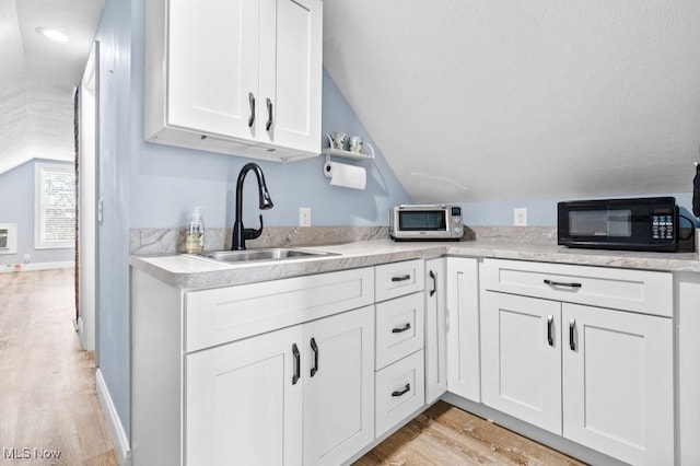 kitchen with black microwave, white cabinetry, a sink, light wood-style flooring, and vaulted ceiling