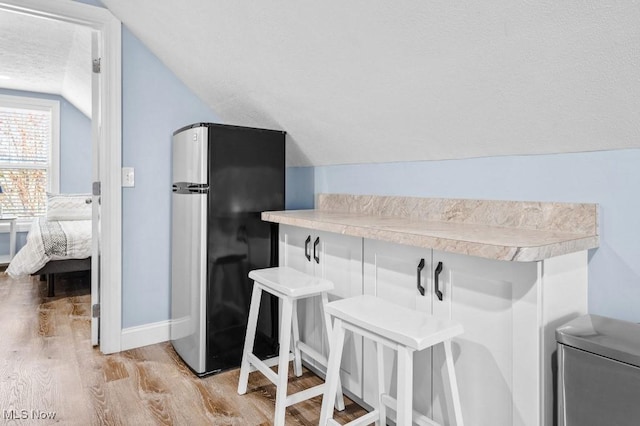 kitchen with freestanding refrigerator, lofted ceiling, a kitchen breakfast bar, light countertops, and light wood-style flooring
