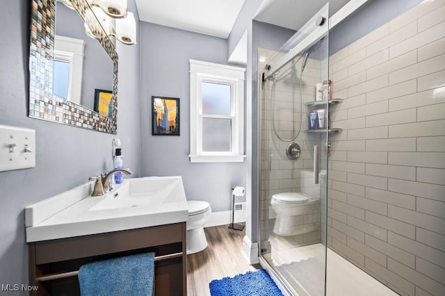 bathroom featuring vanity, wood finished floors, toilet, baseboards, and a stall shower