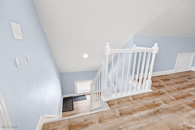 stairway featuring baseboards, wood finished floors, and lofted ceiling