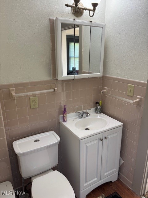 bathroom with tile walls, wainscoting, vanity, toilet, and a textured wall