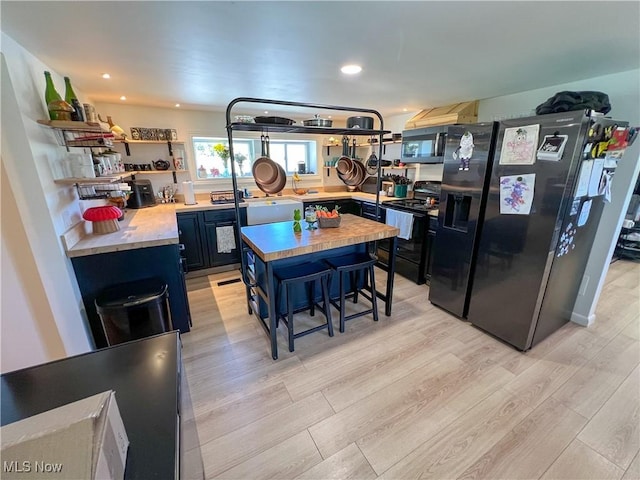 kitchen featuring open shelves, blue cabinetry, a center island, light wood-type flooring, and black appliances