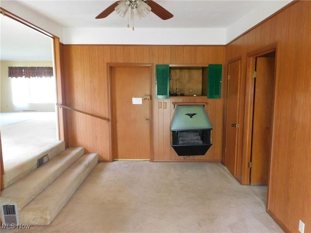 entrance foyer featuring light carpet, wood walls, a ceiling fan, visible vents, and stairway