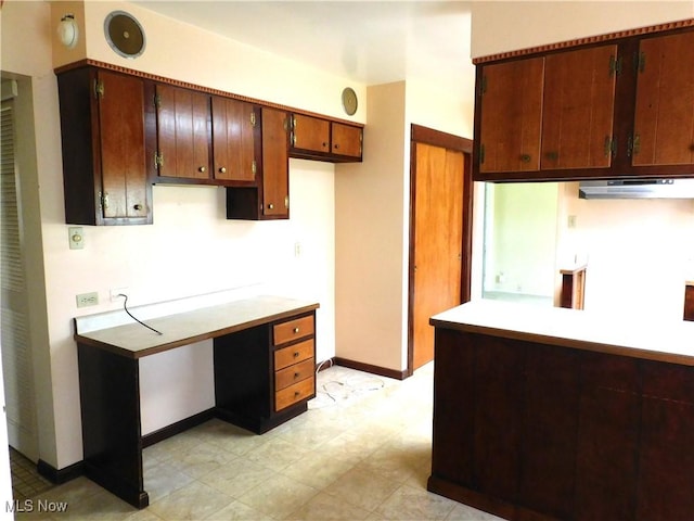 kitchen with baseboards, light countertops, brown cabinetry, and under cabinet range hood