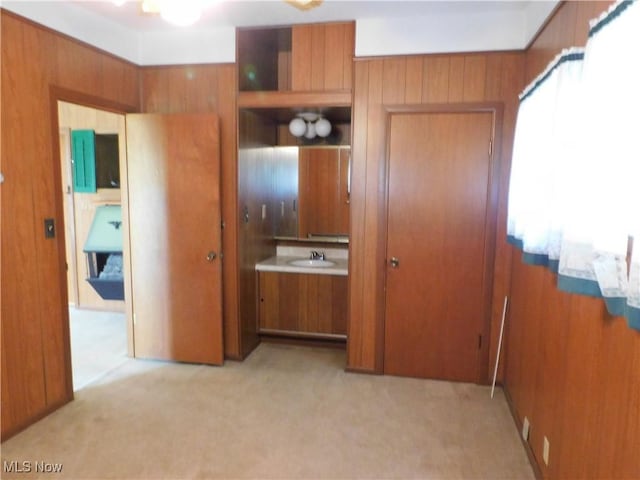 unfurnished bedroom with light colored carpet, a sink, and wooden walls