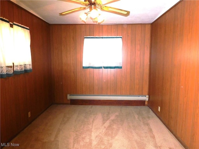 carpeted spare room with a healthy amount of sunlight, ceiling fan, baseboard heating, and wood walls