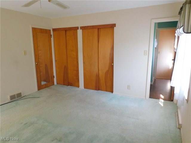 unfurnished bedroom featuring two closets, light colored carpet, a ceiling fan, and visible vents