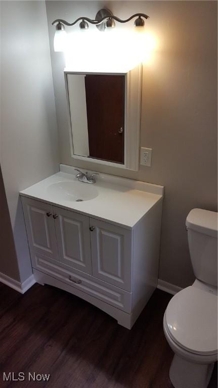 half bath featuring toilet, baseboards, wood finished floors, and vanity
