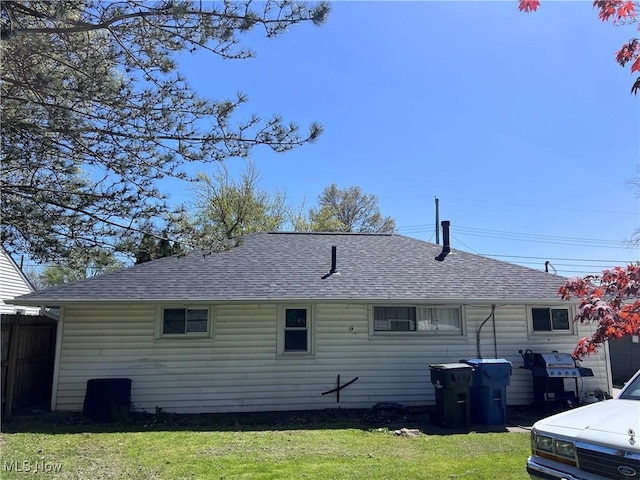 back of property featuring a shingled roof, fence, and a yard