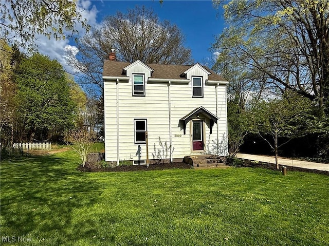 traditional-style house featuring a chimney, a shingled roof, and a front yard