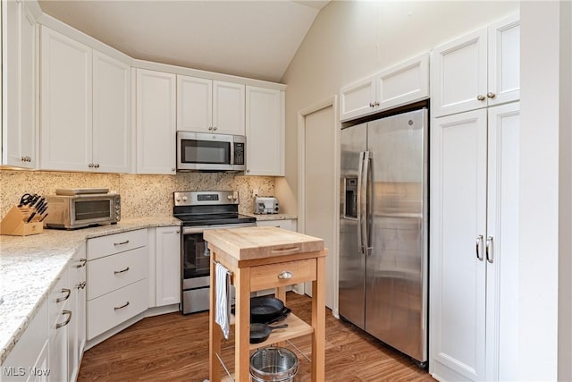 kitchen featuring stainless steel appliances, vaulted ceiling, decorative backsplash, and a toaster