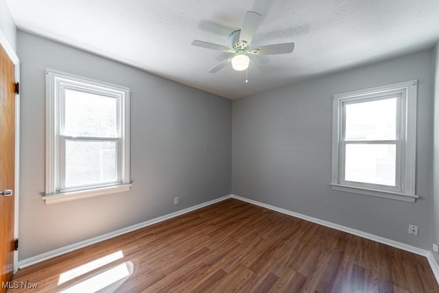 empty room with baseboards, a ceiling fan, wood finished floors, and a healthy amount of sunlight
