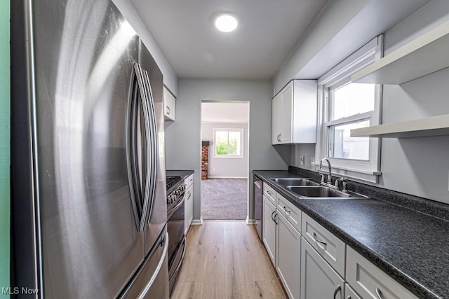 kitchen featuring light wood-type flooring, a sink, appliances with stainless steel finishes, and dark countertops