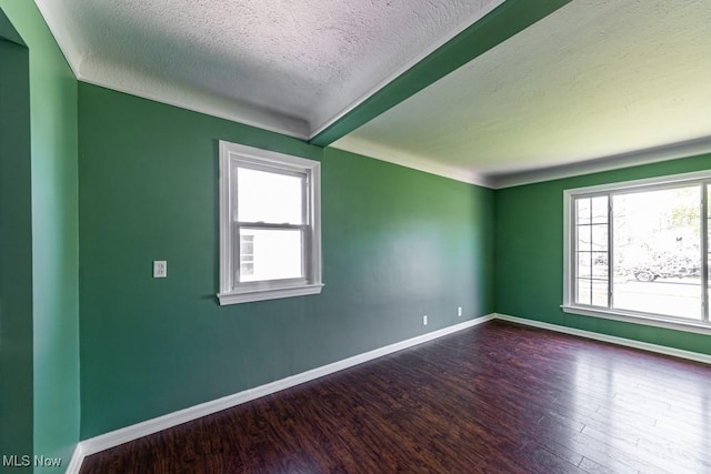 unfurnished room featuring baseboards, beam ceiling, a textured ceiling, and wood finished floors
