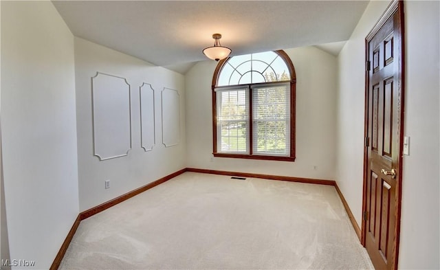 empty room featuring baseboards, visible vents, lofted ceiling, and light colored carpet