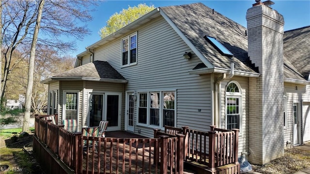 rear view of house featuring roof with shingles, a chimney, and a deck
