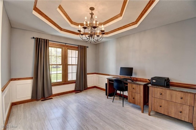 office space featuring crown molding, a notable chandelier, a raised ceiling, light wood finished floors, and a wainscoted wall