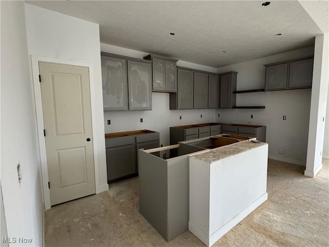 kitchen with a textured ceiling, a kitchen island, and gray cabinetry