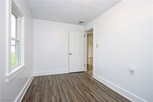 empty room with baseboards, a textured ceiling, dark wood-style flooring, and visible vents