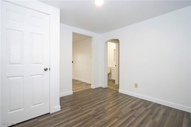 unfurnished room featuring arched walkways, baseboards, and dark wood-type flooring