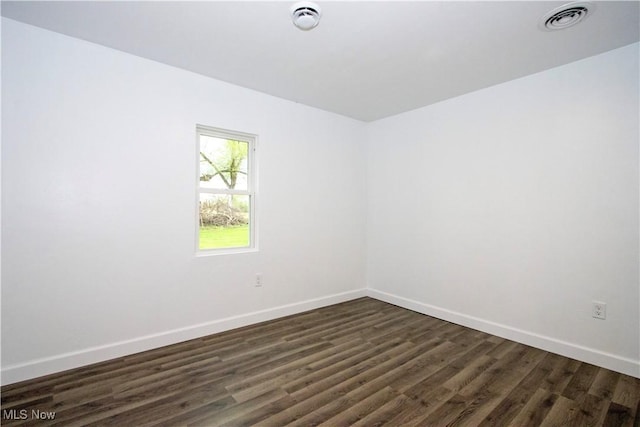 empty room featuring baseboards, visible vents, and dark wood-type flooring