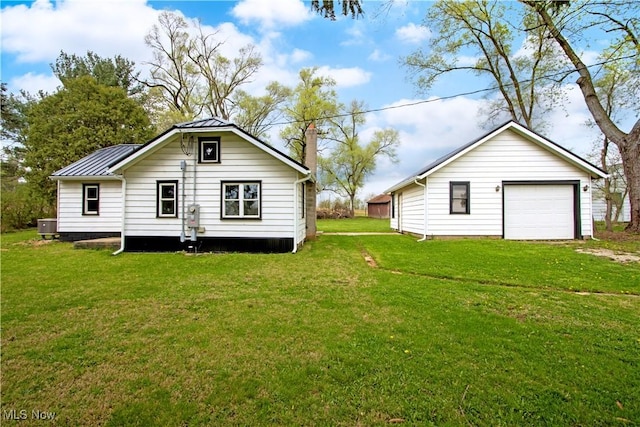 rear view of house with a garage, cooling unit, a chimney, metal roof, and a yard