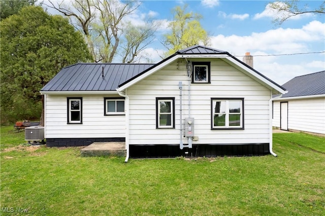 rear view of property with central air condition unit, a yard, a chimney, and metal roof