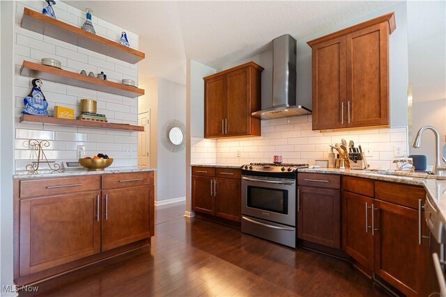 kitchen featuring open shelves, stainless steel gas stove, wall chimney range hood, dark wood-type flooring, and a sink