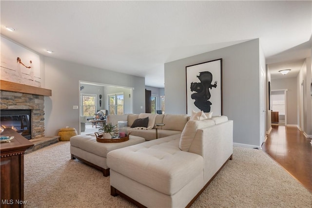 living area with baseboards, a stone fireplace, and wood finished floors