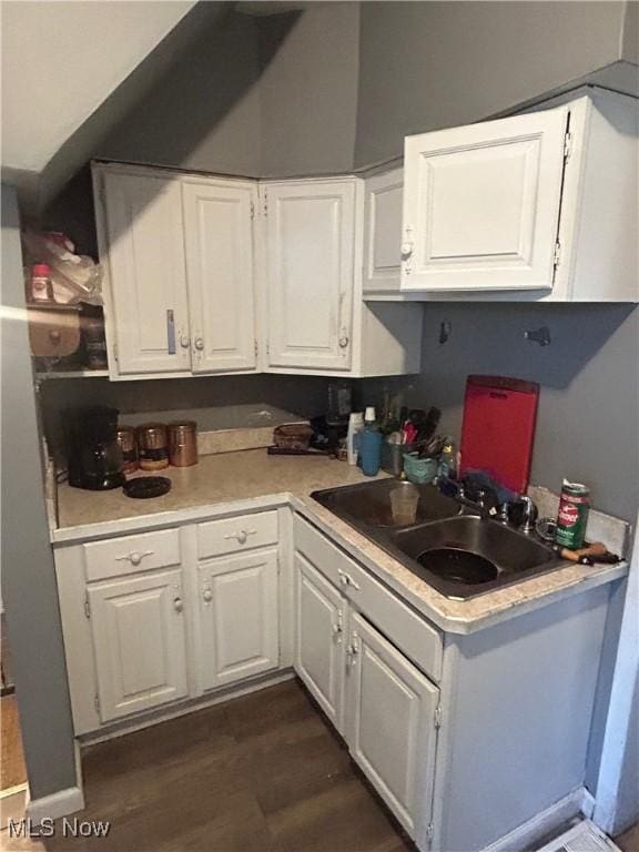 kitchen with light countertops, white cabinetry, a sink, and dark wood-type flooring