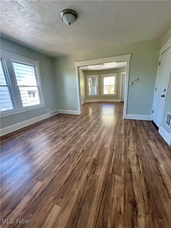 unfurnished living room featuring baseboards, a textured ceiling, dark wood-style flooring, and visible vents