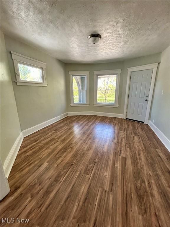 interior space with a textured ceiling, dark wood finished floors, plenty of natural light, and baseboards
