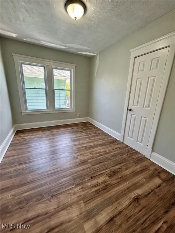 unfurnished room with a textured ceiling, dark wood finished floors, and baseboards