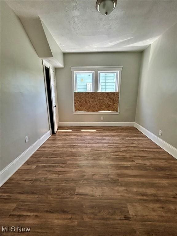 empty room with baseboards and dark wood-type flooring