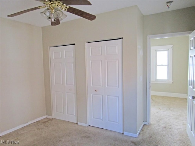 unfurnished bedroom featuring two closets, a ceiling fan, baseboards, and light colored carpet