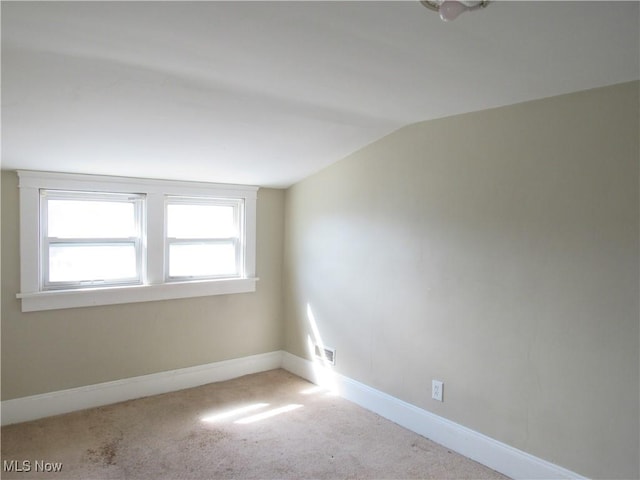 empty room featuring carpet floors, baseboards, lofted ceiling, and visible vents