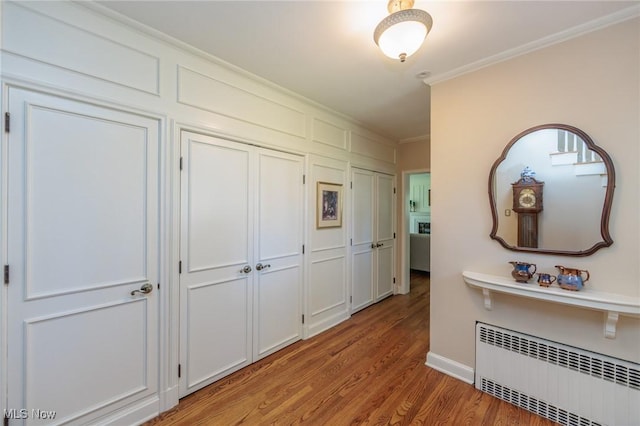 corridor featuring crown molding, baseboards, light wood-style floors, and radiator heating unit